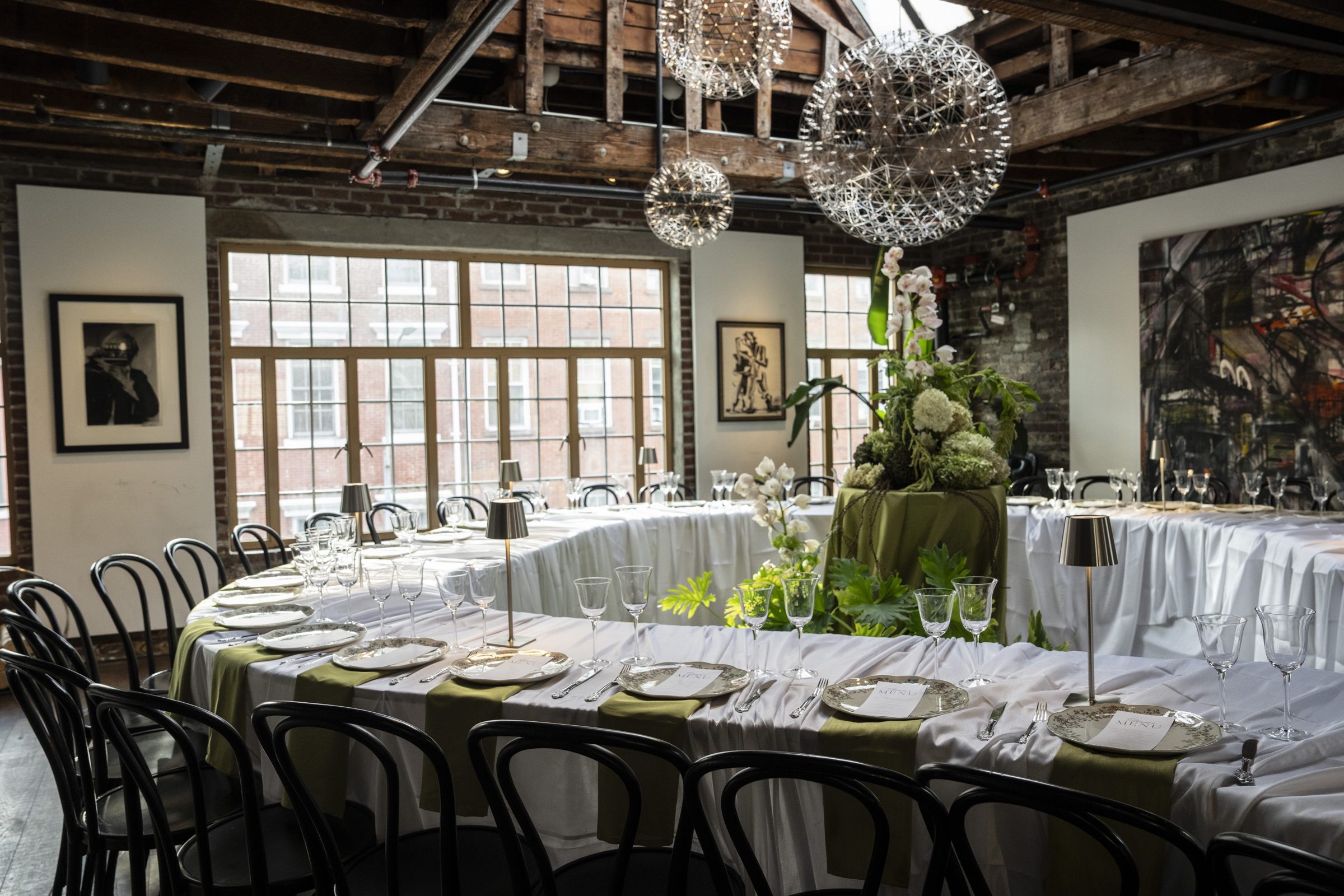 A long dinner table set for an event in a loft with brick walls and glowing pendant lights