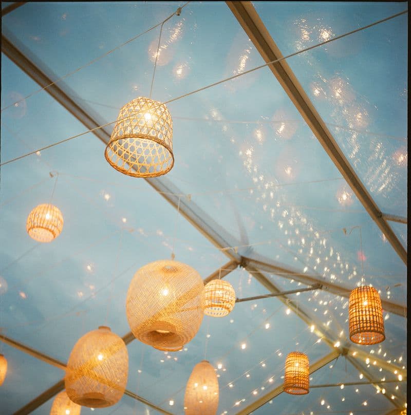 Woven rattan lanterns and string lights strung from a clear-top tent frame